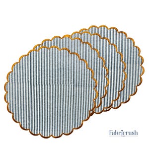 Peut inclure: Quatre sets de table à bordure festonnée. Ils présentent un motif rayé bleu et blanc et une bordure dorée. Les sets de table sont disposés en éventail, se chevauchant légèrement, mettant en valeur leur motif.