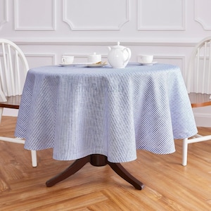 Può includere: Un tavolo rotondo coperto da una tovaglia a righe blu e bianche. Una teiera bianca, due tazze e una zuccheriera sono sul tavolo. Il tavolo ha una base in legno marrone scuro ed è circondato da sedie bianche.