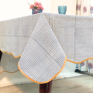 Peut inclure: Une nappe à rayures bleues et blanches avec une bordure orange festonnée. La nappe est drapée sur une table en bois. Un vase de fleurs roses et un verre bleu sont sur la table.