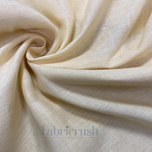 May include: Close-up of a cream-colored linen fabric with visible texture and folds. The fabric has a soft, natural appearance, with the text "Fabricrush" in the lower right corner.