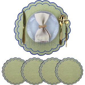 Op de afbeelding: Een gedekte tafel met een lichtgroene placemat met een blauwe geschulpte rand, een wit bord, gouden bestek en een beige servet. Vier bijpassende placemats staan eronder.