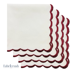 Peut inclure: Quatre serviettes en tissu blanches avec une bordure festonnée bordeaux. Les serviettes sont empilées, mettant en valeur la bordure décorative. Le logo Fabriccrush USA est visible en bas à gauche. Chaque serviette mesure environ 30 cm x 30 cm.