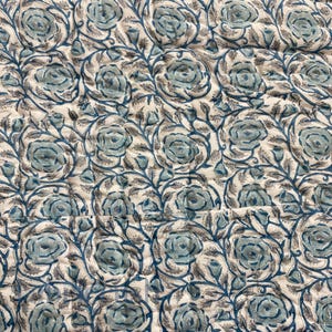 Close-up detail of the Blue Rose Meadow Hand Block Printed Quilt featuring repeating blue rose blooms and leafy vine motifs printed on a soft ivory cotton fabric. The image highlights hand-quilted stitching, gentle texture, and artisanal block print variations, emphasizing the quilt’s handcrafted quality, elegant floral pattern, and timeless, nature-inspired bedding design.