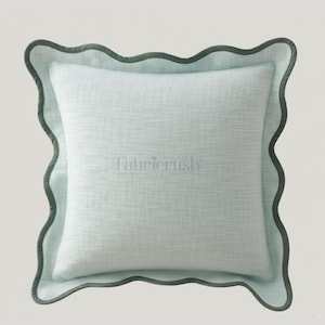 Puede incluir: Un cojín cuadrado azul claro con un borde festoneado en un tono verde azulado más oscuro. El cojín tiene una apariencia texturizada y la palabra "fabricrush" está sutilmente impresa en la parte delantera.