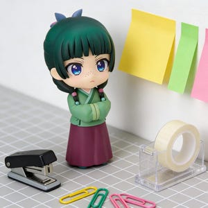 May include: A figurine of a girl with green hair and a green and purple outfit. The figurine has blue eyes and is standing with arms crossed. A stapler, tape dispenser, paper clips, and sticky notes are also in the image.