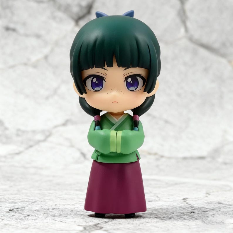 May include: A small figurine of a character with green hair and a matching bow. The figure wears a green top, a long maroon skirt, and has purple eyes. The arms are crossed in front of the chest. The figure has a neutral expression.