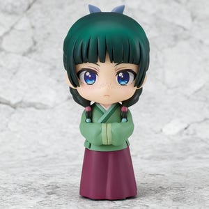 May include: A small figurine of a character with green hair, blue eyes, and a green and maroon outfit. The figure has a stern expression and is posed with arms crossed. The hair is styled with bangs and two braids. A small blue bow is on top of the head.