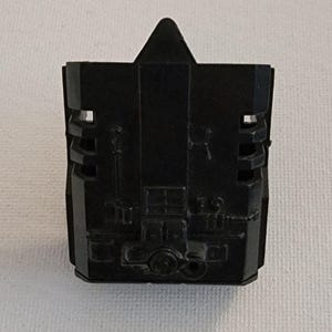 May include: A black plastic component with a geometric design. The object has a triangular top and a rectangular body with various cutouts and circular features. The surface appears matte.