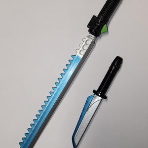 May include: Two toy swords. The larger sword has a black handle with a ridged grip and a blue blade with a serrated edge. The smaller sword has a similar design. Both are on a white surface.