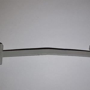 May include: A gray plastic car part, possibly a trim piece or bracket. The part has a long, slightly curved body with detailed, angular ends. The object is set against a plain white background.
