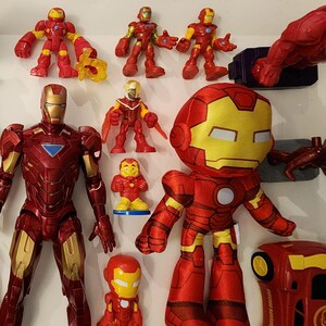 May include: A collection of Iron Man action figures and toys in various sizes and styles. The figures are primarily red and gold, with some featuring yellow accents. The assortment includes a plush toy, plastic figures, and a small car.