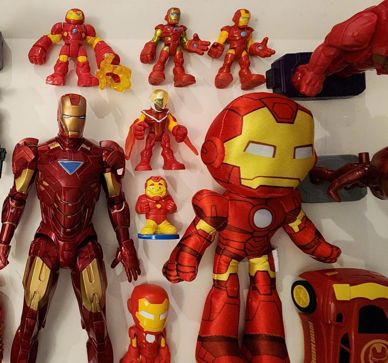 May include: A collection of Iron Man action figures and toys in various sizes and styles. The figures are primarily red and gold, with some featuring yellow accents. The assortment includes a plush toy, plastic figures, and a small car.