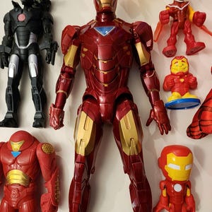 May include: A collection of Iron Man action figures in various sizes and styles. The figures are primarily red and gold, with some featuring black and silver accents. The central figure is a large, detailed Iron Man with a metallic finish.