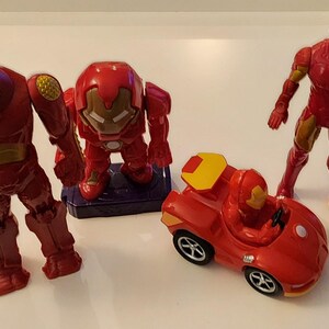 May include: A collection of red and gold Iron Man toys, including two action figures, a small car, and a larger robot-like figure. The toys are made of plastic and are set against a white background.