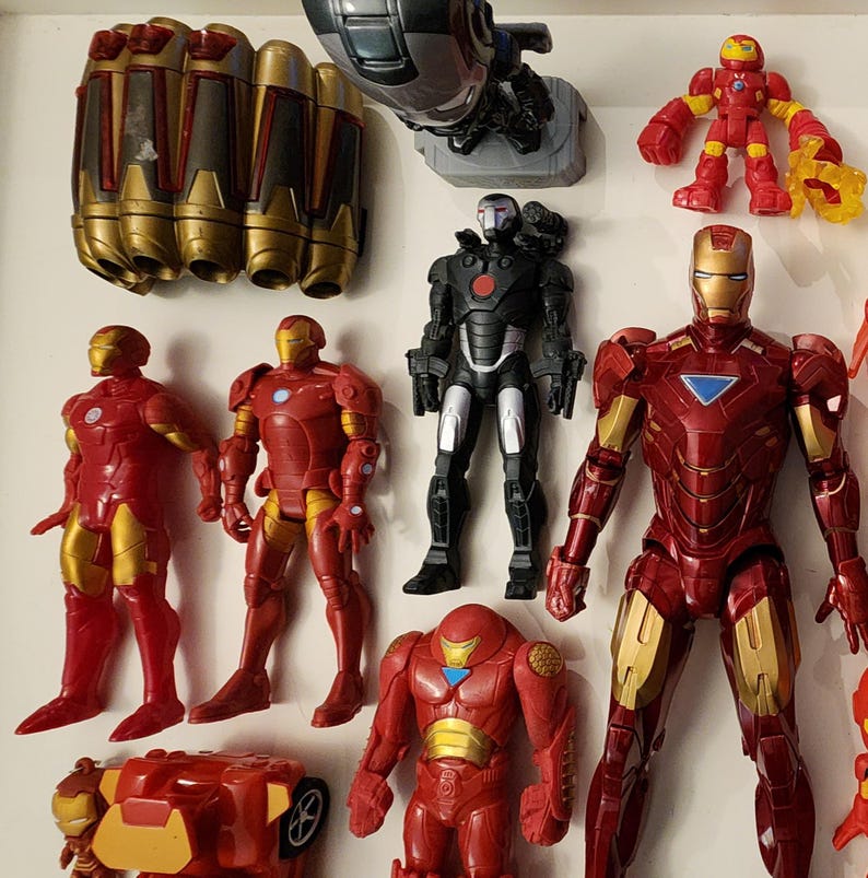 May include: A collection of Iron Man action figures and accessories in various poses. The figures are primarily red and gold, with some black and silver accents. The accessories include gauntlets and a War Machine figure.