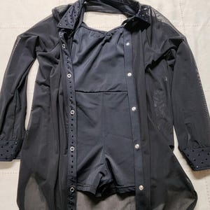以下が含まれることがあります： 黒色のダンスコスチューム。レオタードとシースルーのボタンダウンシャツが特徴です。 シャツは長袖で、袖口と襟にラインストーンのアクセントが付いています。 レオタードは無地の黒色です。