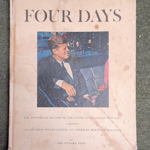 以下が含まれることがあります： ジョン・F・ケネディの肖像画が描かれた「FOUR DAYS」というタイトルのヴィンテージ本の表紙。表紙はシミや摩耗で古くなっています。「THE HISTORICAL RECORD OF THE DEATH OF PRESIDENT KENNEDY」と「UNITED PRESS INTERNATIONAL and AMERICAN HERITAGE MAGAZINE」のテキストが含まれています。