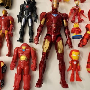 May include: A collection of Iron Man action figures and toys in various sizes and styles. The figures are primarily red and gold, with some black and silver accents. The toys include a plush doll and a toy car.