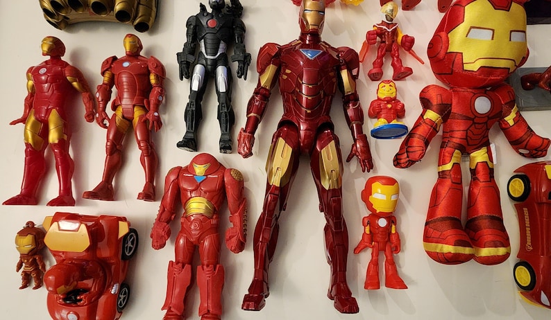 May include: A collection of Iron Man action figures and toys in various sizes and styles. The figures are primarily red and gold, with some black and silver accents. The toys include a plush doll and a toy car.