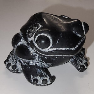 May include: A black frog sculpture with white accents. The frog has large, round eyes and detailed features, including textured skin and webbed feet. This decorative item is a unique piece of home decor.