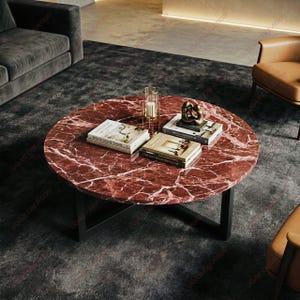 May include: A round coffee table with a red marble top and black metal legs. The table is decorated with books, a candle holder, and a gold sculpture. The table is in a living room setting.
