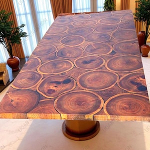 Puede incluir: Una mesa de madera rectangular grande con un dise&ntilde;o &uacute;nico. La tapa de la mesa est&aacute; hecha de numerosas rodajas de madera, creando un patr&oacute;n natural y org&aacute;nico. La mesa est&aacute; soportada por una base de pedestal redonda de madera. El color es marr&oacute;n c&aacute;lido.