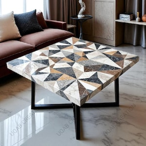 Op de afbeelding: Vierkante salontafel met een geometrisch patroon in tinten wit, grijs, bruin en zwart. Het tafelblad rust op een zwart metalen frame met vier poten. De tafel heeft een modern design.