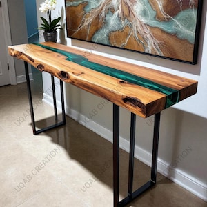Può includere: Una consolle in legno con bordo naturale e un fiume di resina epossidica verde. Il tavolo ha una finitura a venature naturali e poggia su gambe in metallo nero. Il tavolo misura circa 152 cm di lunghezza.