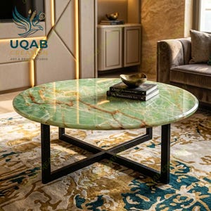 May include: A round coffee table with a polished green onyx stone top featuring natural brown veining and a black metal cross-base frame. A small gold bowl and two stacked books titled Onyx and The Blacksmith's Art rest on the surface.