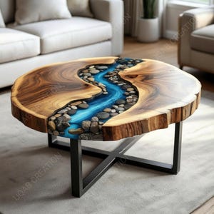 May include: Round wooden coffee table with a river-like blue resin inlay filled with stones. The table has a natural wood edge and sits on a black metal base. A unique piece of furniture for a living room.