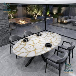 Puede incluir: Una mesa de comedor ovalada con tablero de piedra blanca y vetas doradas, apoyada sobre una base de metal negro. Cuatro sillas tapizadas en gris con estructura negra rodean la mesa, que está dispuesta con platos negros y cubiertos dorados.