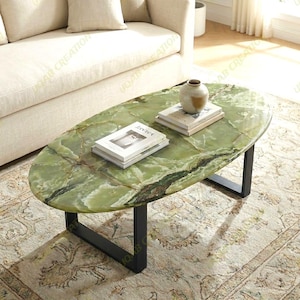 May include: Oval green onyx coffee table with black metal legs. The table has a natural stone pattern and is accessorized with books and a decorative vase. The table is placed on a patterned rug.