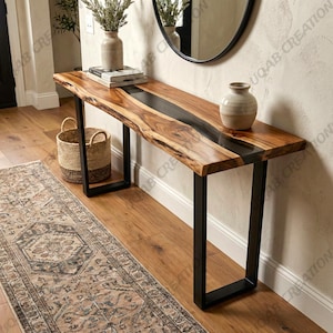 May include: A wooden console table with a live edge design and a black epoxy resin inlay. The table has black metal legs and is decorated with a vase, books, and a woven basket. The table is approximately 152 cm long.