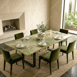 Pode incluir: Um conjunto de sala de jantar com uma mesa retangular de mármore verde com pernas de metal preto, rodeada por seis cadeiras de veludo verde. A mesa está posta com pratos brancos, copos e uma pequena peça central de oliveira. O quarto tem uma paleta de cores neutras.