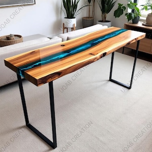 May include: A wooden table with a live edge design and a vibrant blue resin river running through the center. The table has a rectangular shape and is supported by black metal legs. The wood has a natural grain pattern.