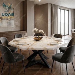 May include: An octagonal dining table with a white marble top featuring gold veining, supported by a black metal X-shaped base. The table is set with white plates, clear glasses, and gold cutlery, with a central bowl containing white flowers.