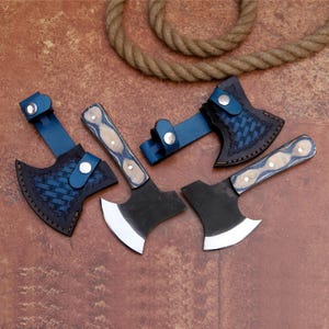 May include: A collection of small axes with black blades and wooden handles with blue and white accents. Each axe has a blue leather sheath with a silver button clasp. A rope is in the background.