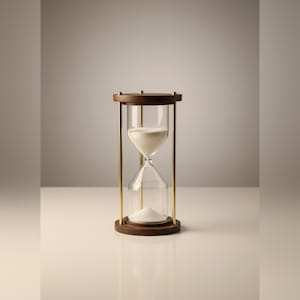 Op de afbeelding: Een zandloper met een donkerbruin houten frame en basis, en goudkleurige metalen steunen. De heldere glazen bol bevat wit zand. De zandloper is een klassiek tijdmeetapparaat, vaak gebruikt voor decoratieve doeleinden.