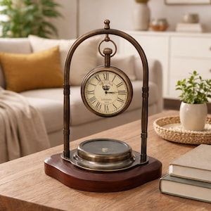 Pode incluir: Um relógio de estilo antigo com base de bússola. O mostrador é creme com algarismos romanos e a inscrição "Victoria London 1915". É suportado por uma estrutura arqueada de cor bronze e assenta numa base de madeira escura.