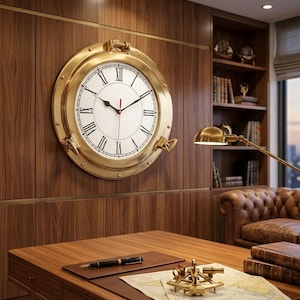 Può includere: Un grande orologio rotondo in ottone con numeri romani e lancette nere è montato su una parete rivestita in legno. L'orologio assomiglia a un oblò di una nave. Sotto c'è una scrivania con una penna, una mappa e strumenti nautici.