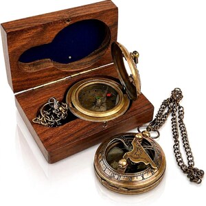 May include: A brass compass with a hinged lid sits inside a rectangular wooden box with a blue velvet lining. A second brass compass with an attached metal chain rests outside the box. Both compasses feature circular dials with markings.
