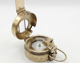 May include: A vintage brass compass with a hinged lid and a clear viewing window. The compass face displays directional markings and a needle. The compass has a ring for attachment and is set against a white background.