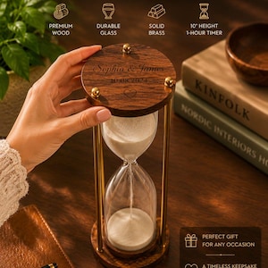 May include: A 25.4 cm tall hourglass with a dark wood base and top, brass pillars, and white sand. The top wooden piece is engraved with the text 'Sophia & James', the date '10.08.2024', and a heart icon. The text 'Personalize Your Time, ENGRAVE YOUR SPECIAL MOMENTS' is visible above.