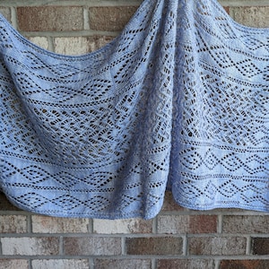 Puede incluir: Un chal de ganchillo azul claro con un delicado patrón de encaje. El chal está drapeado sobre una pared de ladrillo.