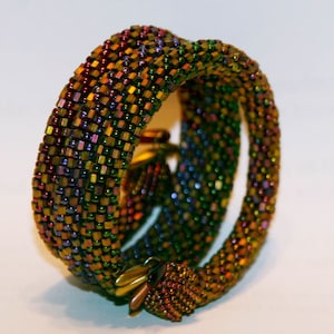 May include: A multi-colored beaded bracelet with a woven design. The bracelet is made of small, iridescent beads in shades of green, purple, red, and gold.