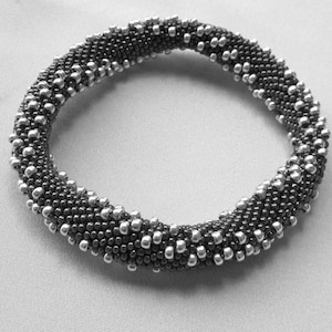May include: A black and silver beaded bracelet with a circular shape. The bracelet is made of small, round beads that are arranged in a pattern.