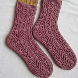 Könnte beinhalten: Ein Paar rosa gestrickte Socken mit einem Zopfmuster.