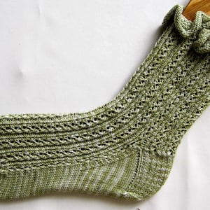 May include: A green and white crocheted sock with a frilled top. The sock is made with a delicate lace pattern.