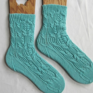 Könnte beinhalten: Ein Paar tealblaue Stricksocken mit einem Zopfmuster. Die Socken werden auf Holzsockensperren gezeigt.