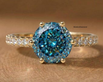 Anillo de compromiso de moissanita talla portuguesa en oro amarillo con banda pavé. Anillo nupcial único con diamantes azul cian. Elegante joya que llama la atención.
